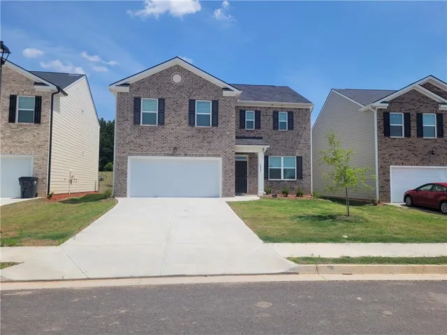 Two-story brick exterior with black shutters, attached two-car garage, and a concrete driveway