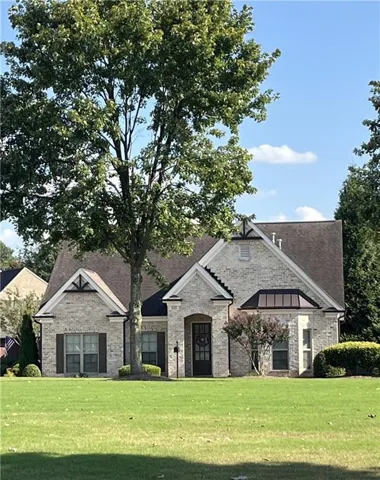 Brick exterior, arched entry, dark brown shutters, manicured landscaping, and a prominent mature tree
