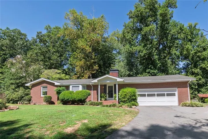Brick exterior featuring a two-car garage, established landscaping, and mature trees