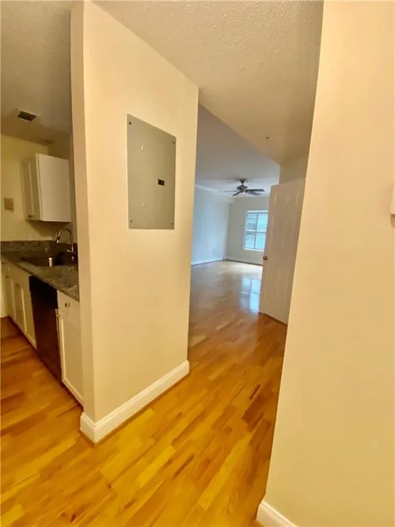 Corridor featuring electric panel, light wood finished floors, a textured ceiling, and lofted ceiling