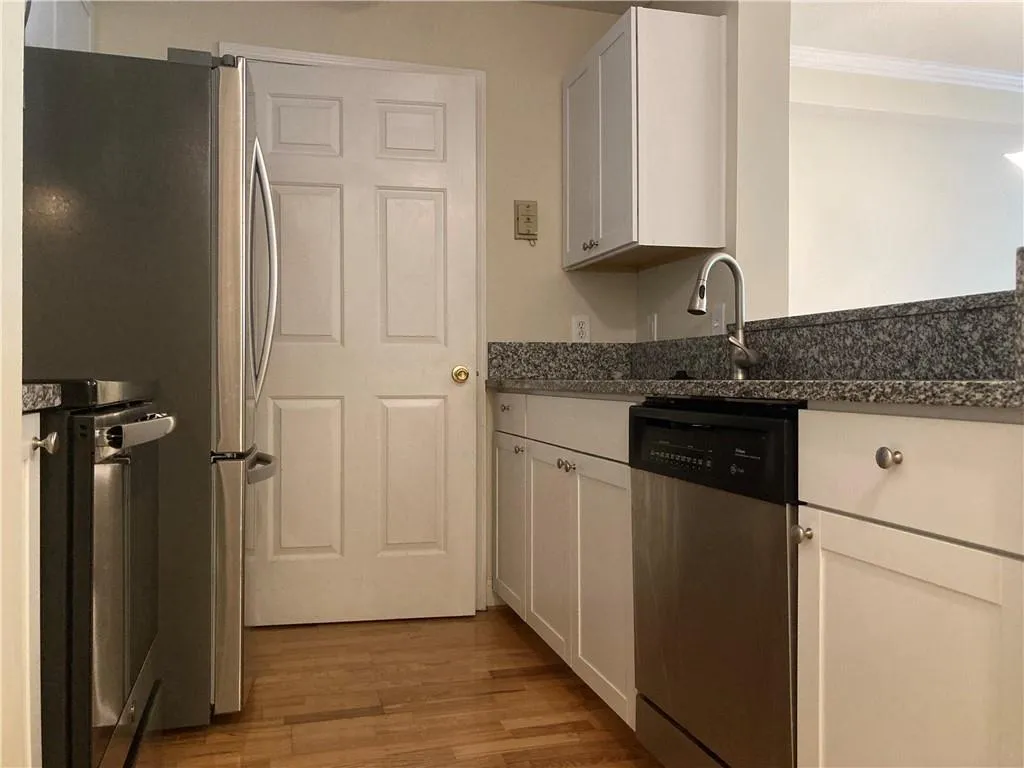 Kitchen with appliances with stainless steel finishes, crown molding, light wood finished floors, white cabinets, and dark stone counters