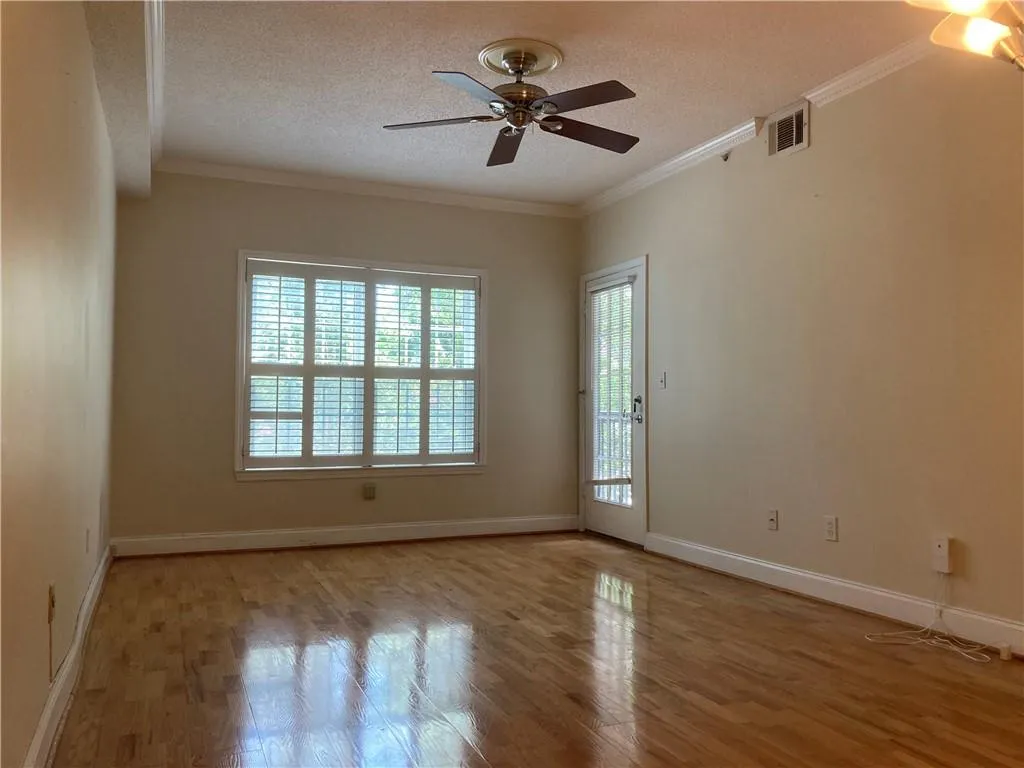 Empty room featuring healthy amount of natural light, ceiling fan, wood finished floors, a textured ceiling, and ornamental molding