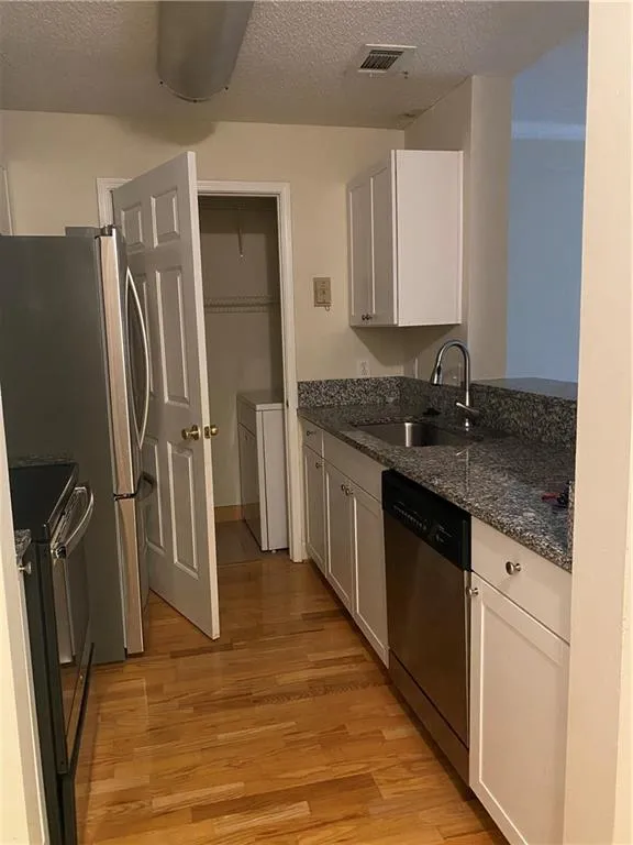 Kitchen featuring dishwashing machine, stove, light wood-type flooring, a textured ceiling, and white cabinetry