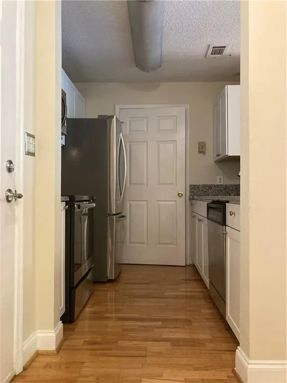 Kitchen featuring range, dishwasher, light wood-style flooring, white cabinets, and a textured ceiling