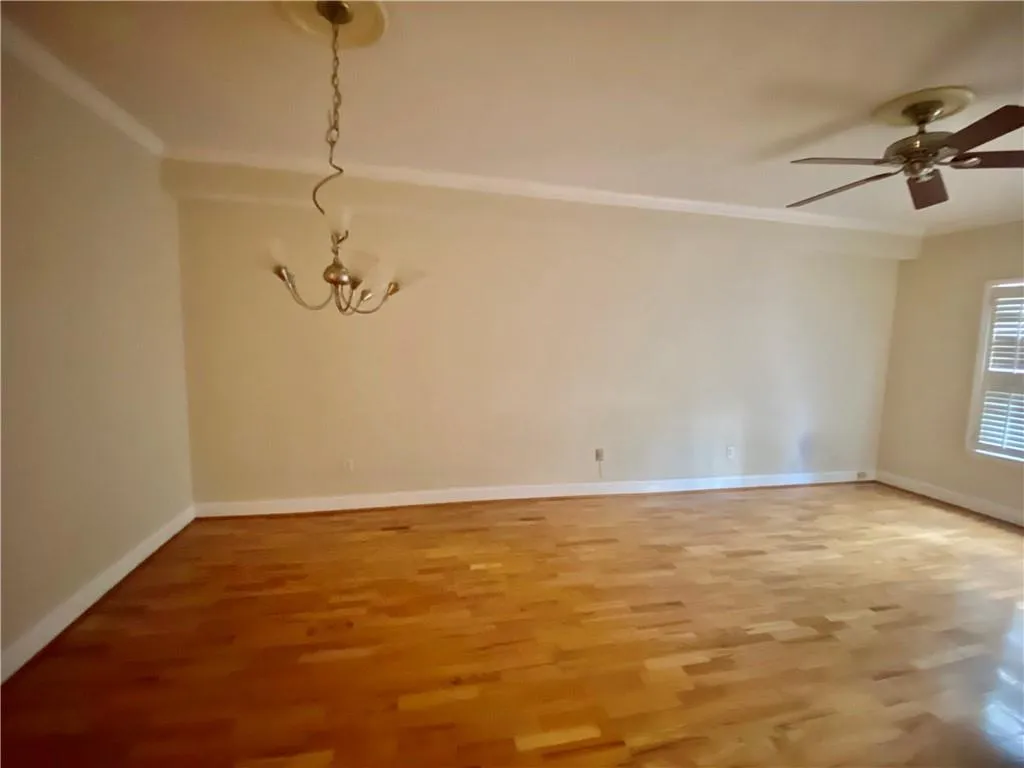 Empty room featuring a ceiling fan, ornamental molding, light wood-type flooring, and a chandelier