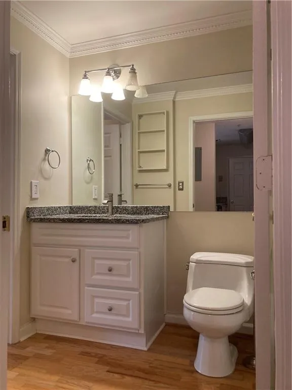 Half bath with wood finished floors, vanity, and ornamental molding