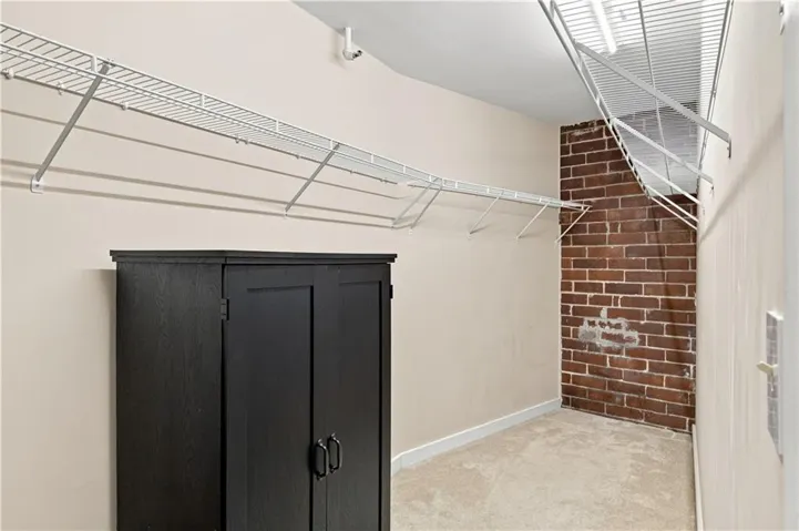 Spacious walk-in closet featuring wire shelving, exposed brick detail, and light-colored carpeting