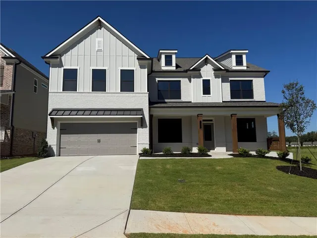 Two-story residence featuring a combination of white painted brick and vertical siding, a two-car garage with a metal awning, and a covered entry with wood-finish columns