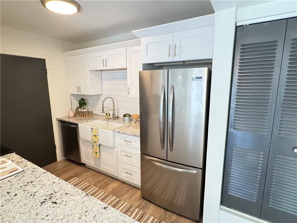 Kitchen featuring light stone countertops, white cabinetry, stainless steel appliances, hardwood / wood-style floors, and decorative backsplash