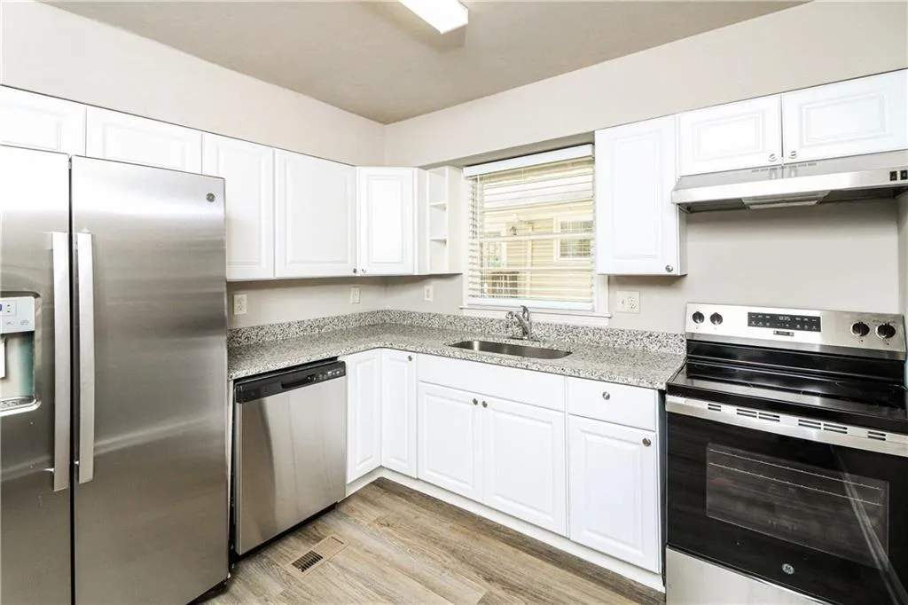 Kitchen featuring appliances with stainless steel finishes, under cabinet range hood, white cabinets, light wood-style flooring, and light stone counters
