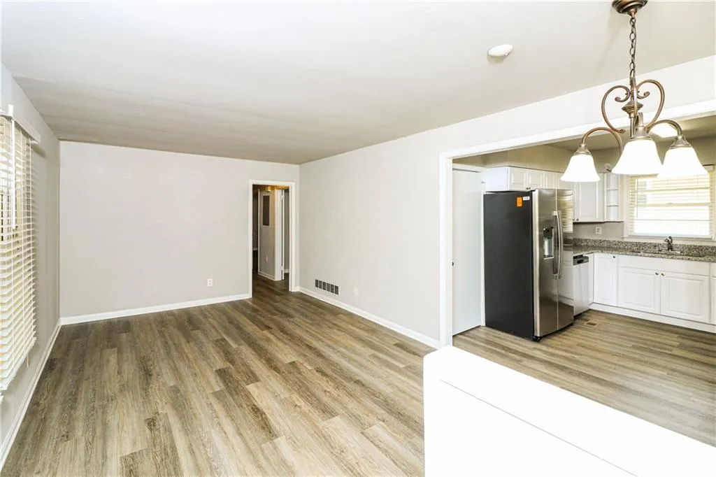 Kitchen with appliances with stainless steel finishes, wood finished floors, white cabinets, open floor plan, and pendant lighting