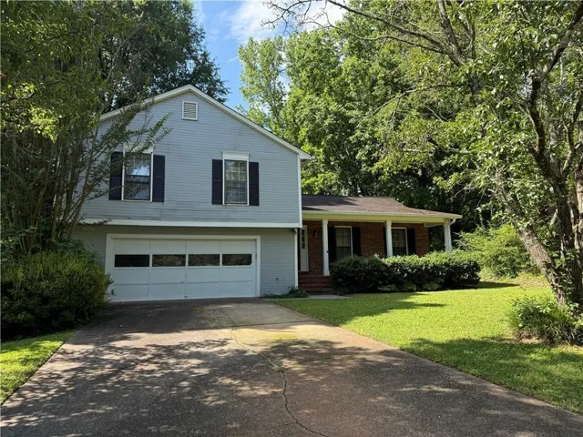 Two-story residence featuring light blue siding, a two-car garage with paneling, and a covered front porch with white columns