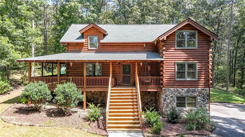 Log cabin exterior with a covered front porch, stone foundation, and wood-finish siding