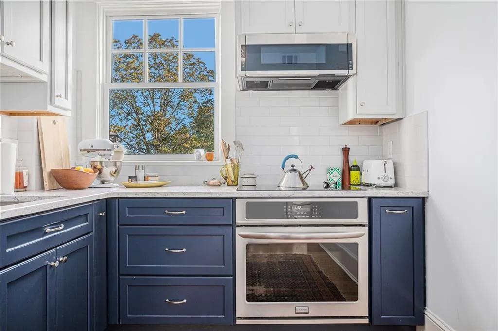 Kitchen featuring blue cabinets, white cabinetry, appliances with stainless steel finishes, and decorative backsplash