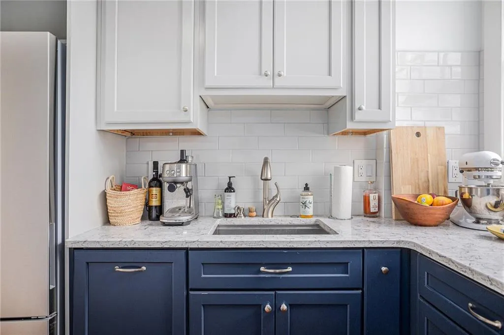 Kitchen with blue cabinets, sink, stainless steel refrigerator, decorative backsplash, and white cabinets