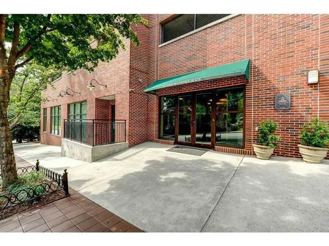 Brick exterior featuring an awning over glass entry doors, concrete walkways, and planted containers