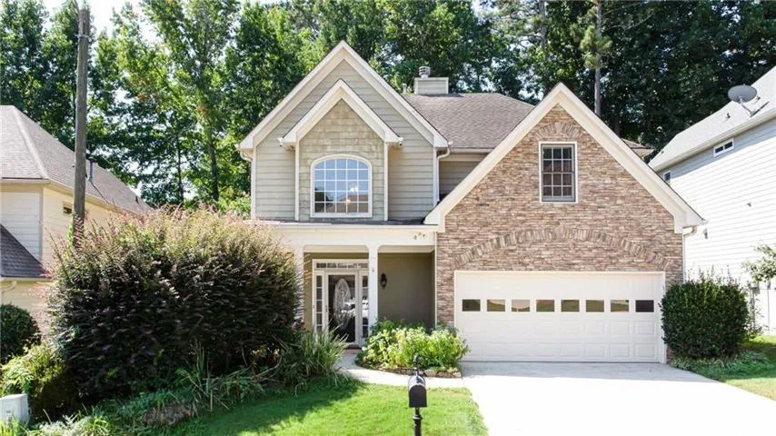 Two-story residence featuring a shingled roof, partial stone facade, and a two-car garage