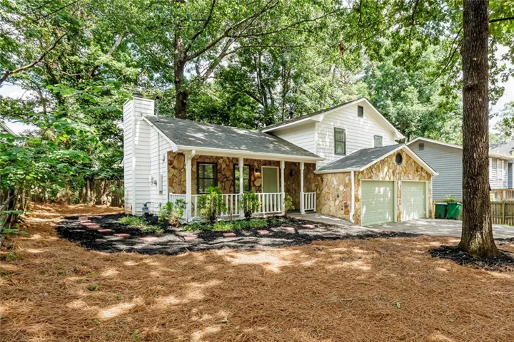 Stone façade accents, front porch with white railing, a two-car garage, and established tree coverage