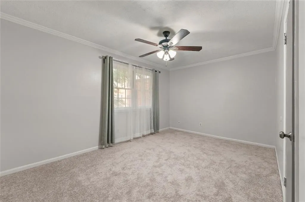Spare room featuring ceiling fan, ornamental molding, and light colored carpet Spare room featuring ceiling fan, ornamental molding, and light colored carpet