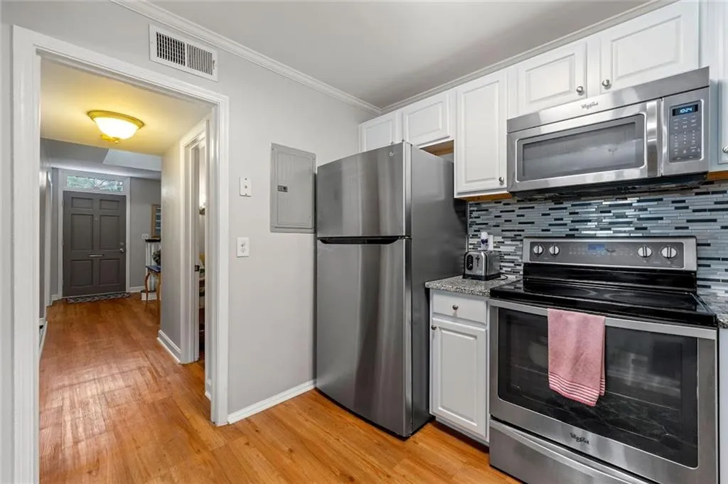 Kitchen featuring white cabinetry, ornamental molding, light hardwood / wood-style floors, appliances with stainless steel finishes, and backsplash Kitchen featuring white cabinetry, ornamental molding, light hardwood / wood-style floors, appliances with stainless steel finishes, and backsplash