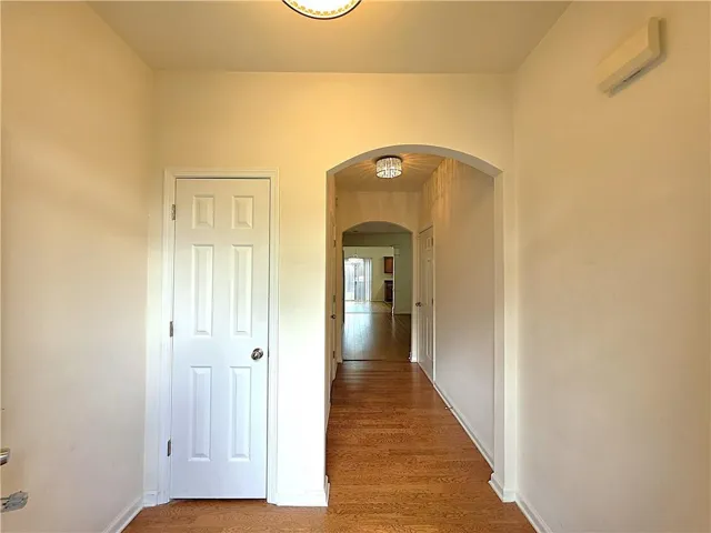 Wood-finish flooring extending through an arched hallway, featuring light-toned walls and a six-panel interior door