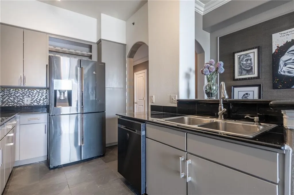 Kitchen with arched walkways, stainless steel fridge with ice dispenser, dark countertops, crown molding, and dishwashing machine