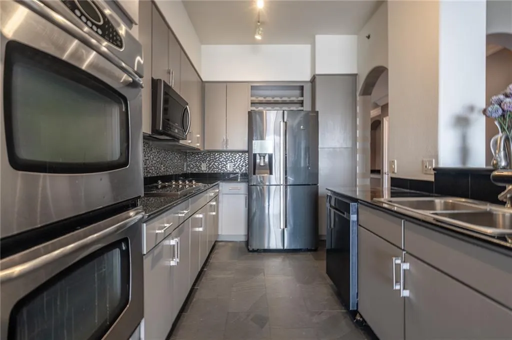 Kitchen with appliances with stainless steel finishes, arched walkways, dark countertops, gray cabinets, and backsplash