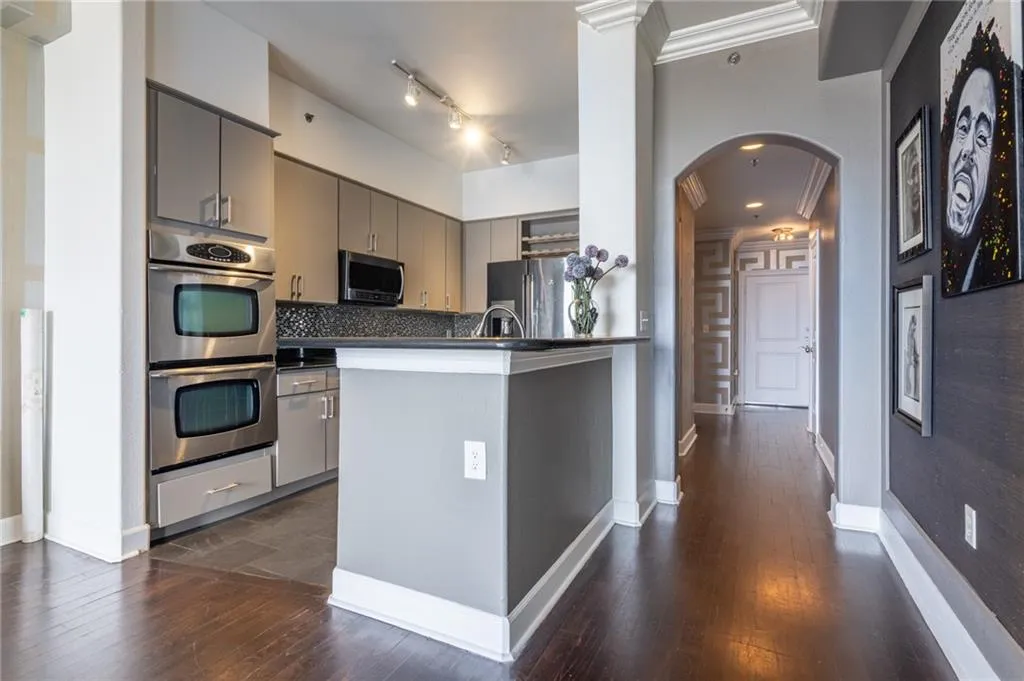 Kitchen with gray cabinets, arched walkways, appliances with stainless steel finishes, dark countertops, and tasteful backsplash