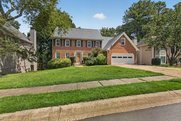 Brick exterior, two-car garage, mature trees, landscaped front yard, and a concrete driveway