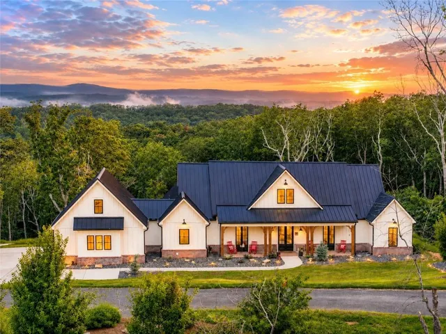 Modern farmhouse exterior with a dark metal roof, white vertical siding, and stone accents