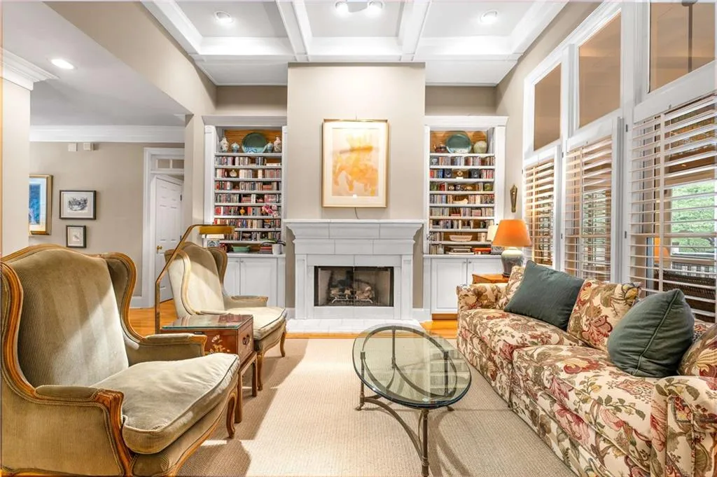 Expansive living room has floor to ceiling windows, a gas fireplace with gas logs, built in bookshelves, and coffered 11 foot ceilings
