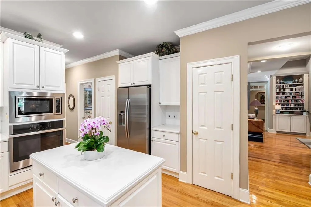 Kitchen features white cabinets and white countertops, a peninsula and an island, gas cooktop, stainless steel wall oven,  built-in microwave, side by side refrigerator, and multiple pantry closets