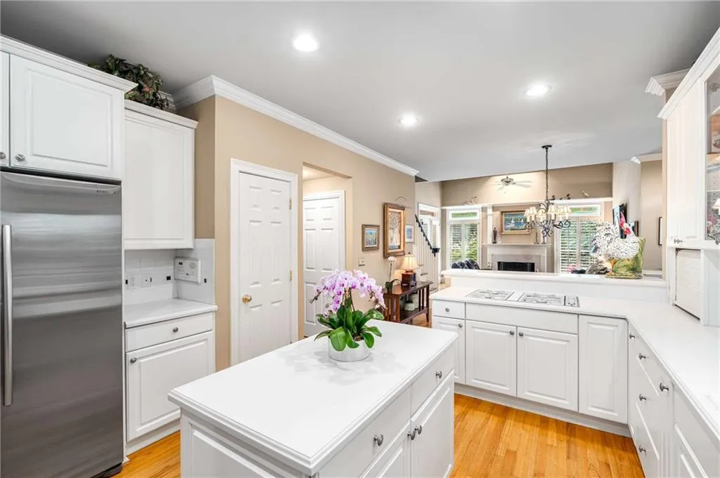 Kitchen features white cabinets and white countertops, a peninsula and an island, gas cooktop, stainless steel wall oven,  built-in microwave, side by side refrigerator, and multiple pantry closets