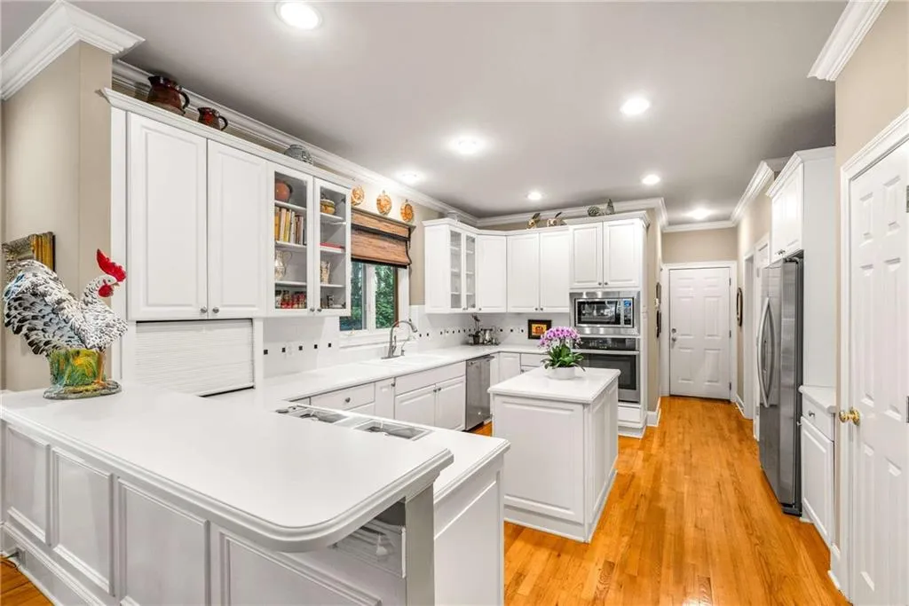 Kitchen features white cabinets and white countertops, a peninsula and an island, gas cooktop, stainless steel wall oven,  built-in microwave, side by side refrigerator, and multiple pantry closets
