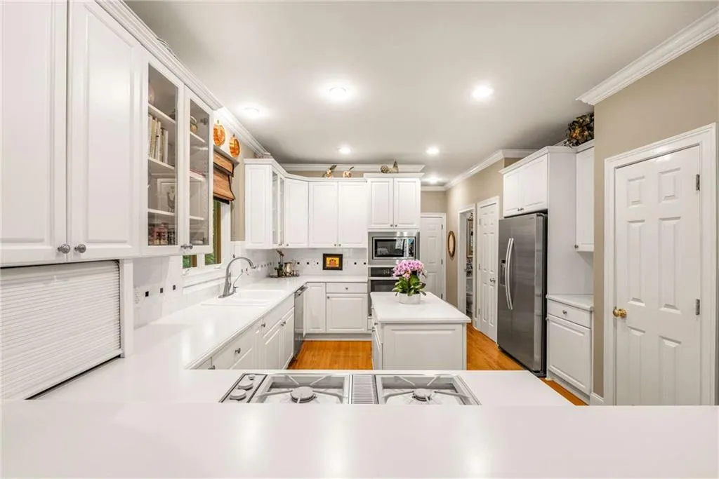 Kitchen features white cabinets and white countertops, a peninsula and an island, gas cooktop, stainless steel wall oven,  built-in microwave, side by side refrigerator, and multiple pantry closets
