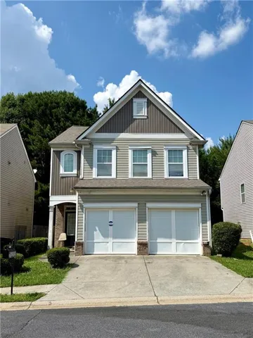 Two-story residence featuring light gray siding with contrasting brown vertical siding accents, a two-car garage, and a peaked roofline