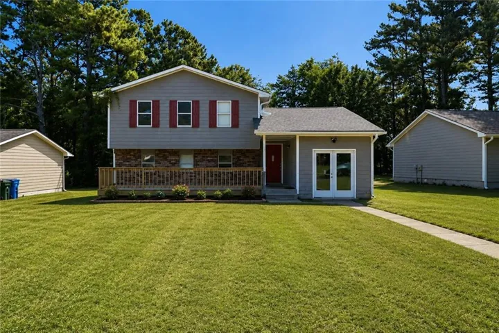 Split-level residence featuring gray siding, a red entry door, and white double French doors