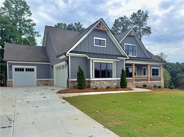 Craftsman-style exterior featuring gray siding, a brick foundation, a covered porch with wood columns, an attached two-car garage, and a concrete driveway