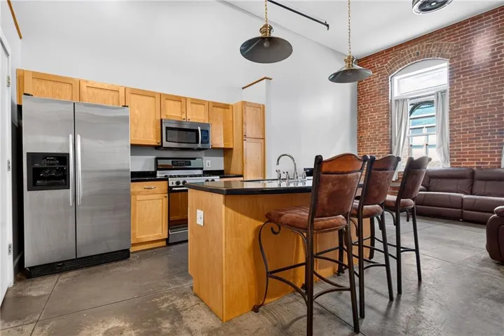 Kitchen featuring stainless steel appliances, wood cabinetry, dark countertops, and an island with bar seating
