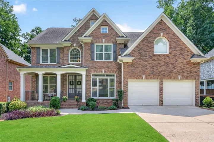 Brick exterior featuring a two-car garage, covered porch, arched windows, and mature landscaping