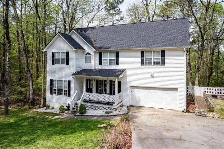 Traditional home with a porch, a garage, concrete driveway, a front yard, and a shingled roof
