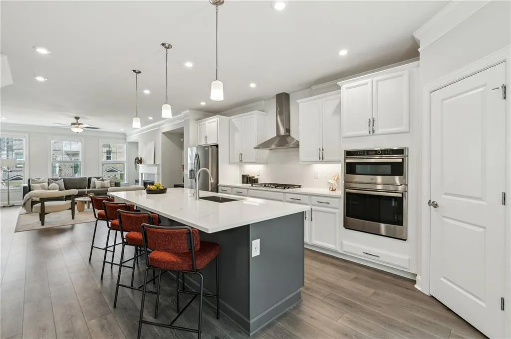 Kitchen with an island with sink, wall chimney range hood, a kitchen bar, wood finished floors, and white cabinetry