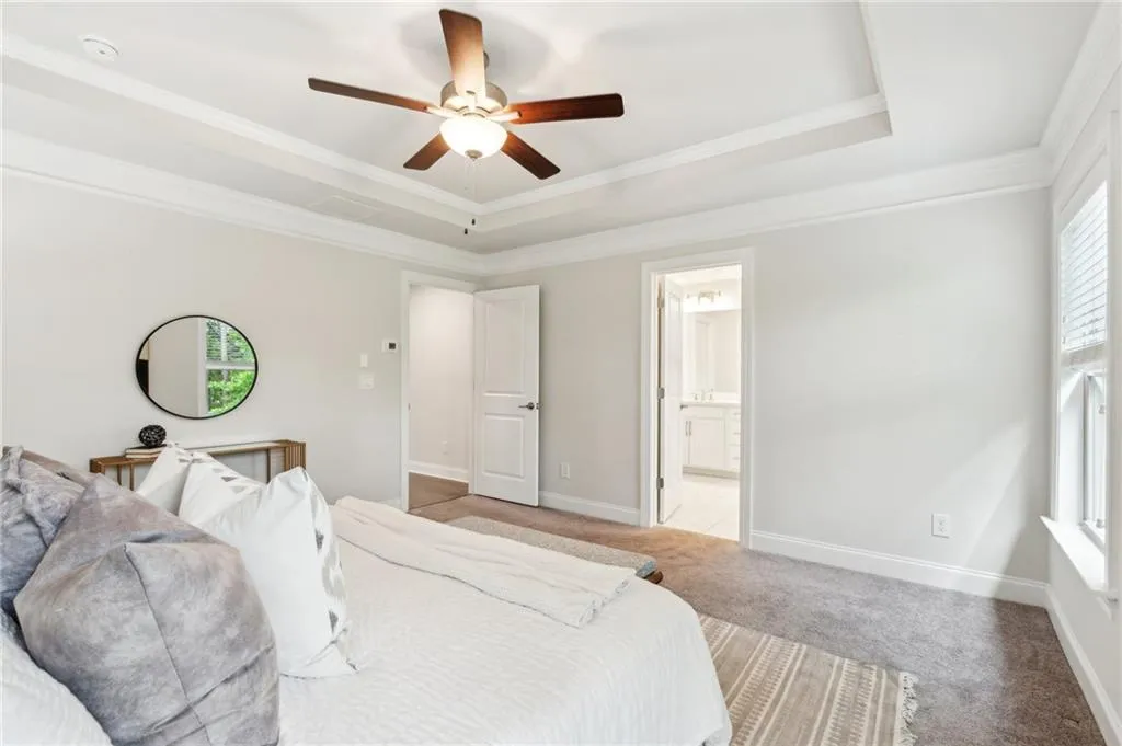 Bedroom featuring multiple windows, light colored carpet, a tray ceiling, crown molding, and ensuite bath