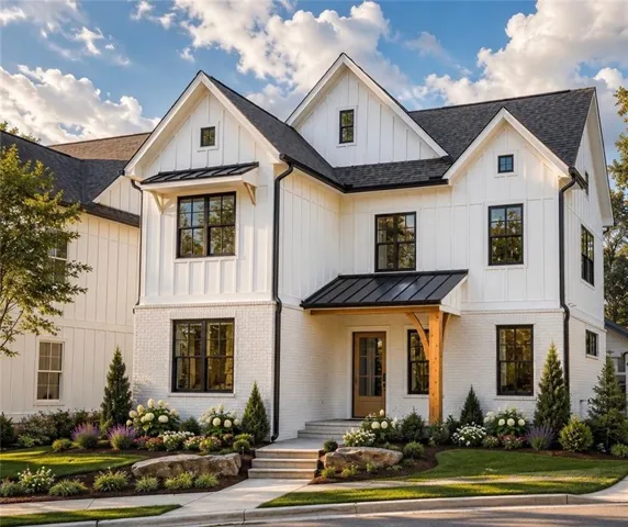 Modern farmhouse exterior featuring white board-and-batten siding with white painted brick accents, black-framed windows, dark asphalt shingle roofing, and a front entry with a wood door and a metal awning supported by a wood beam
