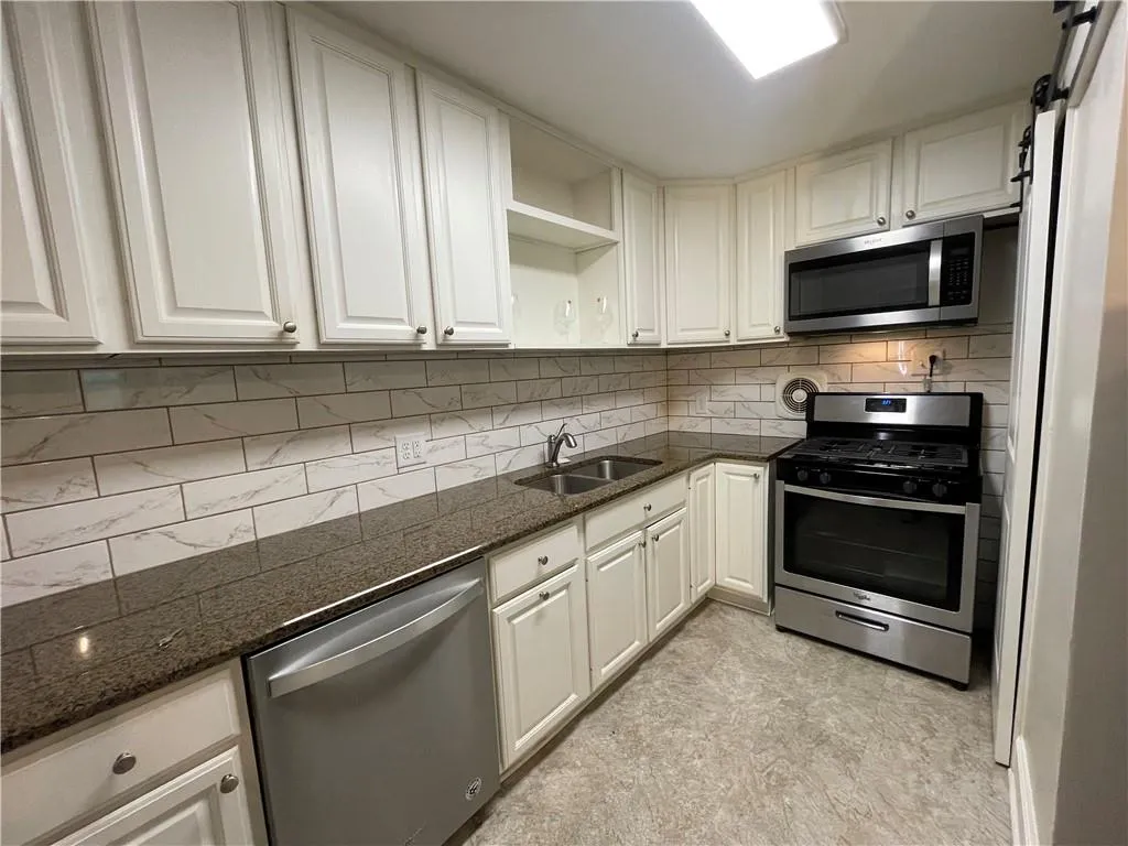 Kitchen with appliances with stainless steel finishes, open shelves, decorative backsplash, dark stone counters, and white cabinetry