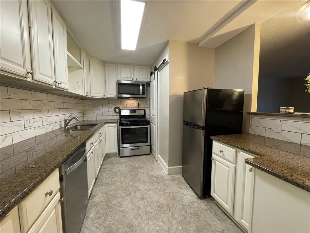 Kitchen featuring a barn door, open shelves, tasteful backsplash, appliances with stainless steel finishes, and dark stone countertops