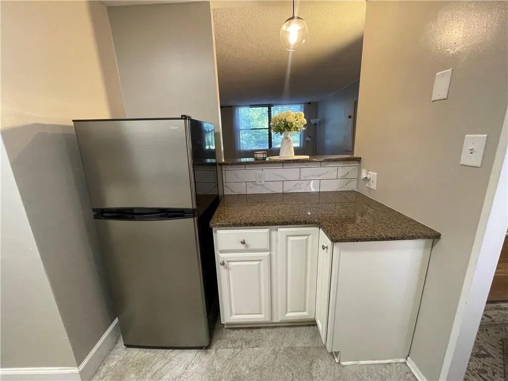 Kitchen featuring freestanding refrigerator, white cabinetry, dark stone countertops, hanging light fixtures, and tasteful backsplash
