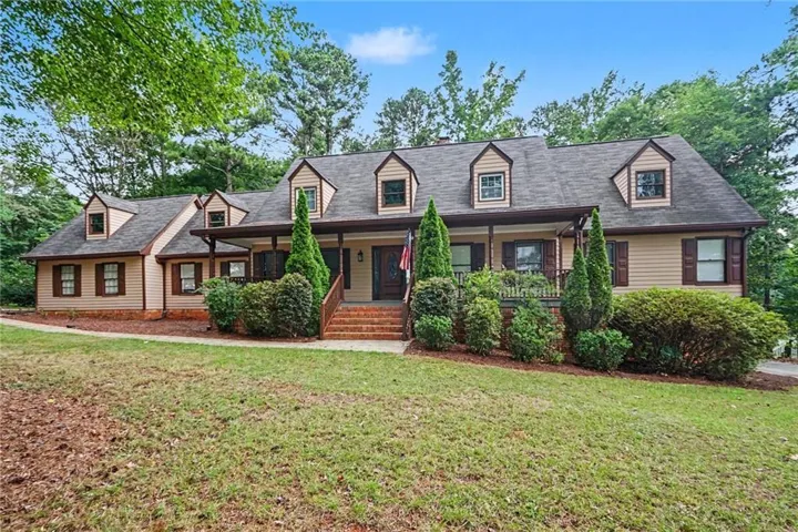 Traditional-style residence featuring a dormered roofline, neutral siding, and dark shutters