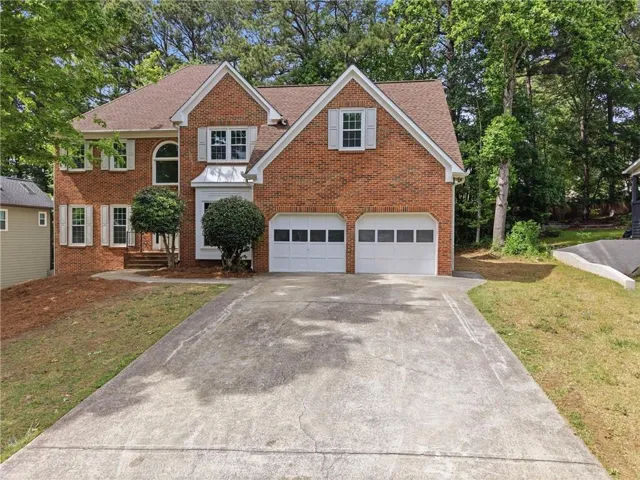 Brick-clad residence featuring a two-car garage, multiple gables, and white shuttered windows