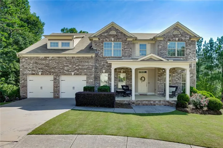 Two-story brick and stone Colonial featuring a columned front porch with arched entryway, dual two-car garages, and manicured lawn with mature landscaping